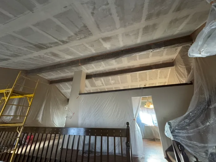 Taped and mudded ceiling between wood beams, room in plastic