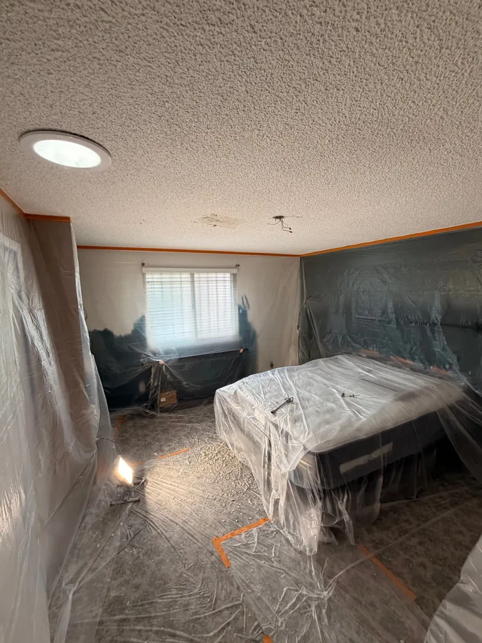 Bedroom with popcorn ceiling, furniture covered in plastic