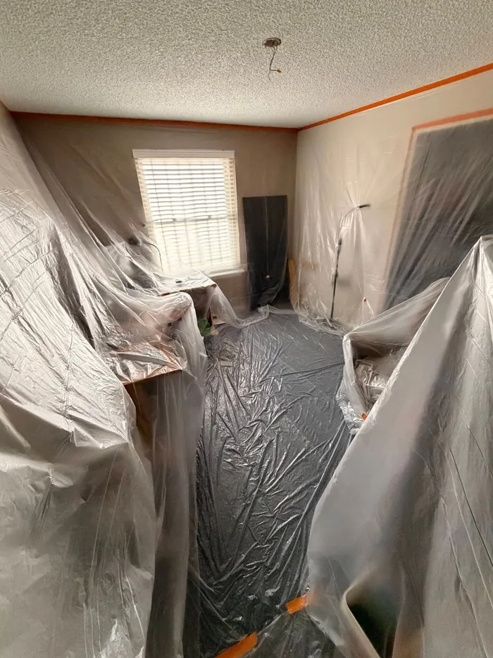 Office with popcorn ceiling, walls and floor covered in plastic